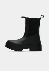 Botine negre până la gleznă, cu un superior din piele texturată, panouri laterale elastice și mânere pentru tragere. Talpă groasă din cauciuc cu un design masiv și textură striată.