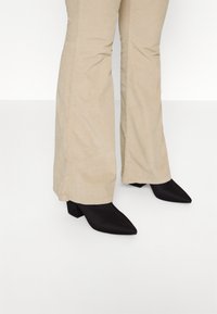 Svarta spetsiga ankelboots med klack och tjock klack, kombinerade med krämfärgade sammetsbyxor med utsvängda ben och vertikal ribb.