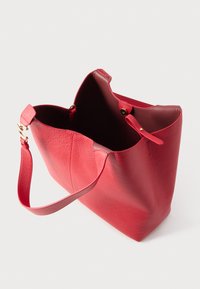 Punane nahast käekott tekstuurse pinnaga. Omab avatud ülaosa, reguleeritavat rihma ja sisemist nööpkinnitust.