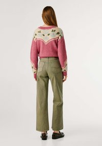 Suéter rosa difuso con patrón floral y cuello en contraste, combinado con jeans de pierna ancha de talle alto en verde oliva y zapatos oscuros.