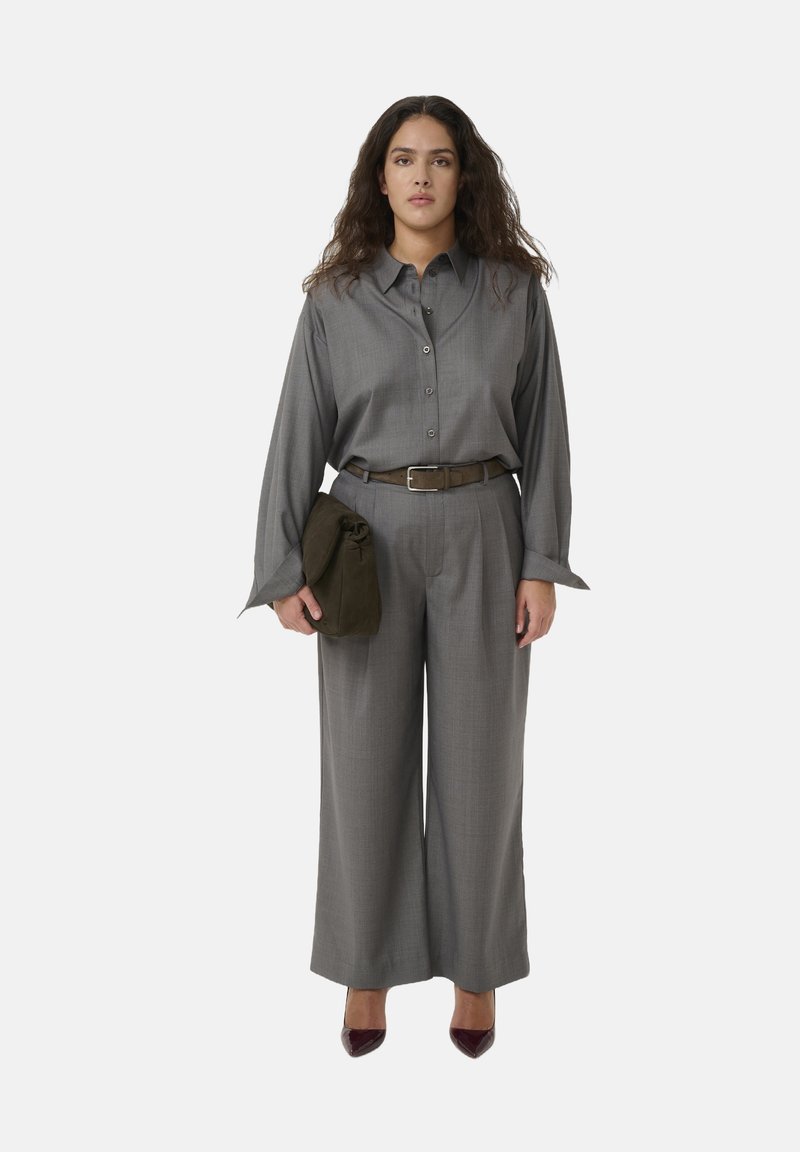 Graues Hemd mit weitem Arm, kombiniert mit hochgeschnittenen grauen Hosen. Abgerundet mit einer grünen Clutch und burgunderfarbenen Absatzschuhen.