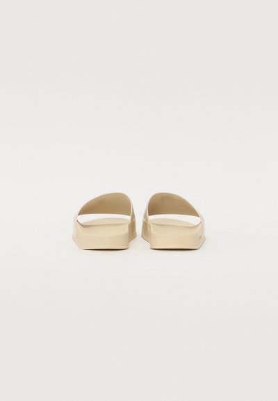Beige slidesandaler med åben tå og to buestropper. Fremstillet af glat, fleksibelt materiale med en flad, tekstureret sål.
