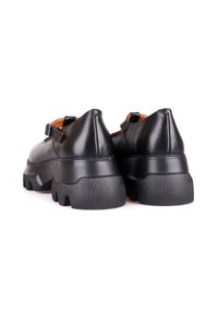 Paire de chaussures à plateforme en cuir noir avec semelles épaisses à rainures et brides à la cheville, vues de dos sur un fond blanc.