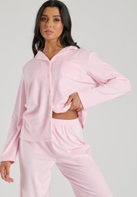 Lyserød pyjamas sæt med en knap-op top, der har en brystlomme og lange ærmer, kombineret med løstsiddende bukser med elastisk talje.