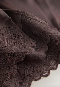 Tissu en dentelle marron foncé avec motifs floraux et bords festonnés sur un fond lisse en matière assortie.