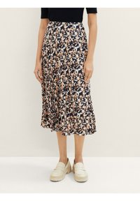 Jupe midi florale avec un fond bleu marine, ornée de fleurs pêches et blanches. Design plissé, associée à des mocassins plateforme beiges.