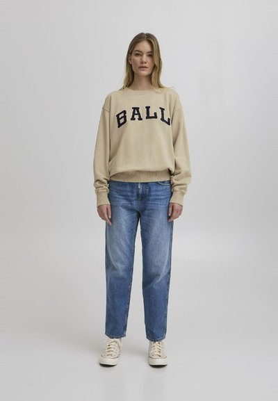 Beige genser med "BALL" i mørkeblå bokstaver, kombinert med lyseblå jeans. Passformen er avslappet, og stoffet ser mykt ut.