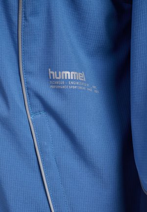 Blauw gestructureerde stof met reflecterende bies en "hummel" logo, inclusief tekst "Techwear ontwikkeld door HMI, performance sportkleding sinds 1923."