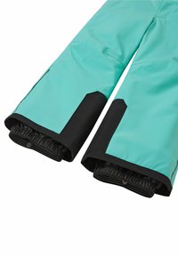 Pantalons imperméables en turquoise avec des accents noirs. Dotés d'une taille élastique et de poignets réglables avec des zips pour un ajustement sécurisé.