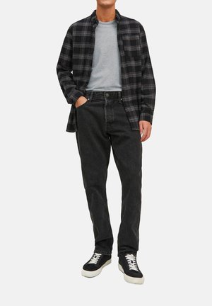 Zwart geblokt overhemd over een grijs T-shirt, gecombineerd met donkere jeans en zwarte sneakers met witte veters. Simpele, casual gelaagde outfit.