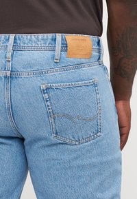 Jeans de denim azul claro con una textura suave, que cuentan con una etiqueta de cuero marrón en la cinturilla y un bolsillo trasero con costuras sutiles.