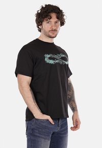 T-shirt in cotone nero con una grafica di simbolo dell'infinito color turchese sul petto. Maniche corte, scollatura rotonda, vestibilità morbida. Tessuto testurizzato.