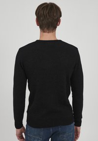 Dunkelgrauer Strickpullover mit Rundhalsausschnitt, gerippten Bündchen und Saum. Glatte Textur, mittleres Gewicht und lässige Passform, kombiniert mit blauen Jeans.