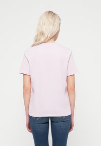 Ροζ βαμβακερό t-shirt με κοντά μανίκια και στρογγυλή λαιμόκοψη, συνδυασμένο με μπλε τζιν παντελόνι. Η πίσω όψη δείχνει έναν απλό σχεδιασμό.