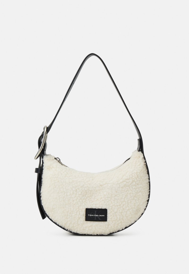 Petit sac d'épaule en peau lainée blanche en forme de croissant avec sangle noire et écusson du logo Calvin Klein Jeans sur le devant.