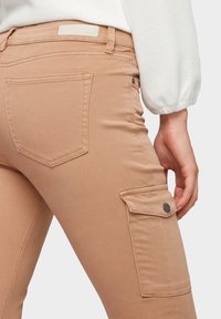 Pantalones cargo beige de corte ajustado, con un bolsillo lateral, bolsillos traseros y una textura suave. Fabricados en una mezcla de algodón elástico.
