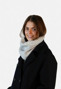 Sciarpa infinita grigia in maglia, avvolta in modo semplice, con una sottile trama a coste e un piccolo etichetta, abbinata a un cappotto nero.