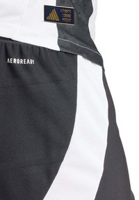 Pantaloni sportivi bianco e nero con tessuto testurizzato, branding AEROREADY e un badge logo Adidas in un colore oro a contrasto.