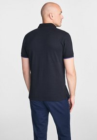 Czarna koszulka polo z krótkim rękawem, z kontrastowymi fioletowymi akcentami przy mankietach i klasycznym kołnierzykiem. Gładka tekstura, regularny krój.