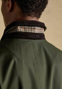 Rückansicht einer Person, die eine dunkelgrüne Jacke mit einem schwarzen Cordkragen trägt, der mit kariertem Stoff gefüttert ist.