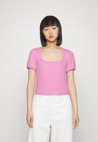 Top rosa de mangas curtas e canelado com decote quadrado. Design ajustado com mangas bufantes. Combinado com calças brancas de perna larga.