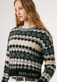 Gebreide trui met een geometrisch patroon in zwart, grijs en beige, met een ronde halslijn en geribbelde zoom, gemaakt van zachte materialen.