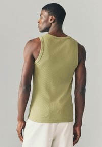 Top de tirantes acanalado en verde oliva con escote redondo, diseño ajustado y amplias sisas. Costuras visibles y una textura suave.