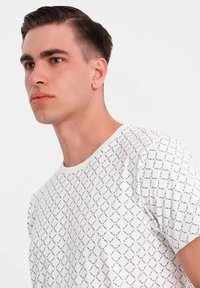 Bílá tričko s černým geometrickým vzorem, kulatý výstřih, krátké rukávy, vyrobené z měkké látky, s texturovaným designem.