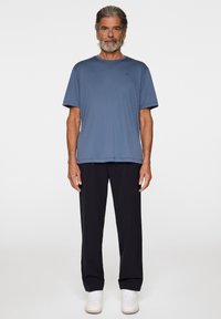 Blå kortärmad T-shirt med rund hals, i kombination med svarta byxor och vita skor. Enkel, avslappnad passform med en mjuk textur.