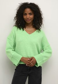 Hellgrüner, oversized Pullover mit V-Ausschnitt, breiten Rippenbündchen und weicher Textur. Kombiniert mit dunklen Jeans hat er lässige Ärmel.