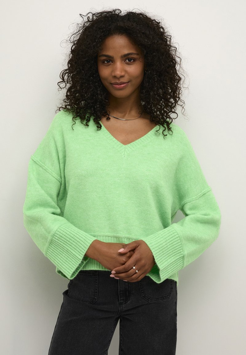 Hellgrüner, oversized Pullover mit V-Ausschnitt, breiten Rippenbündchen und weicher Textur. Kombiniert mit dunklen Jeans hat er lässige Ärmel.