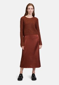 Maglione a maglia color ruggine con collo rotondo e maniche lunghe, abbinato a una gonna midi in satin ruggine liscia e scarpe chunky nere con plateau.