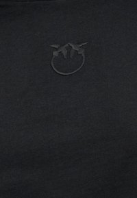 Μαύρο ύφασμα με διακριτικό κεντητό έμβλημα δύο πουλιών που κοιτούν το ένα το άλλο πάνω από έναν κύκλο.