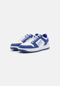 White and blue sneakers with a smooth leather upper, perforated toe box, lace-up front, and rubber sole. Features logo patch on the side.