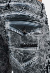 Jeans in denim con una finitura grigia sbiadita, dotati di un design decorativo sulla tasca posteriore, patch con logo e dettagli di cucitura a contrasto.