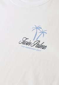 Tissu blanc avec un motif graphique bleu clair de deux palmiers et un texte manuscrit noir "Twin Palms" au-dessus du texte bleu "The Barefoot Edit".