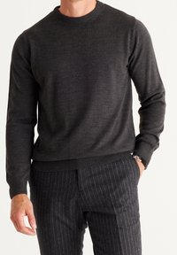 Dunkelgrauer Rundhalsausschnitt-Pullover aus einem glatten Stoff, mit gerippten Bündchen und Saum. Kombiniert mit gestreiften, dunkelgrauen Hosen.