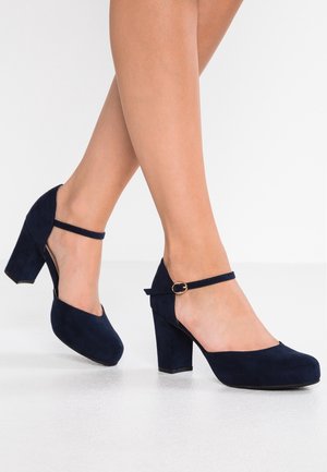 Granatowe zamszowe szpilki z okrągłym noskiem, paskiem wokół kostki i słupkowym obcasem. Charakteryzują się wycięciami oraz złotym zapięciem.