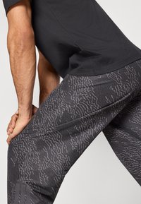 Μαύρο T-shirt συνδυασμένο με γκρι αθλητικό παντελόνι που διαθέτει υφή με κυματιστό μοτίβο και τρεις κάθετες ρίγες στο κάτω μέρος του ποδιού.