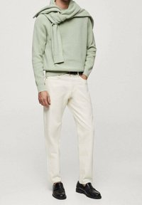 Hellgrüner, gerippter Pullover, über die Schultern getragen, kombiniert mit cremeweißen Jeans und schwarzen Loafers. Einfaches Design, weiche Textur und kontrastreiche Farben.