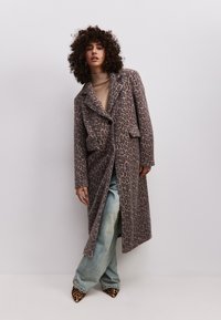 Leopardenmuster langer Mantel aus weichem, strukturiertem Stoff, mit Reverskragen, Knopfverschluss und Seitentaschen. Kombiniert mit hellblauen Jeans.