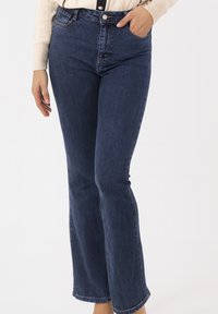 Donkerblauwe denim flared jeans met een hoge taille, voorzien van een knoopsluiting, riemlussen, voorzakken en een licht vervaagde afwerking.