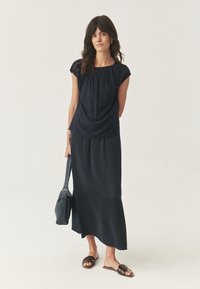 Blusa blu navy con scollo arricciato, abbinata a una lunga gonna maxi nera e fluida. Indossata con sandali marroni e portando una borsa a tracolla nera.