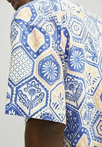 Korte mouwen shirt met een hexagonaal patroon in blauw en beige, voorzien van bloemmotieven en geometrische ontwerpen. Gemaakt van textuurstof.
