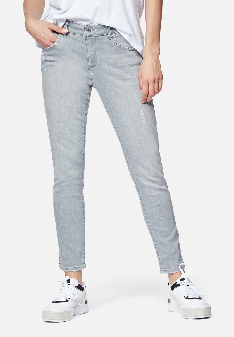 Vaqueros ajustados de color gris claro, fabricados en denim, con una cintura de altura media, ligero desgastado y diseño de cinco bolsillos, combinados con zapatillas blancas.