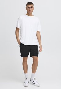 Vit T-shirt med rund halsringning, svarta shorts med fickor, som bärs med vita sneakers och vita strumpor. Enkelt, avslappnat snitt, utan mönster eller dekorationer.