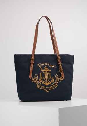 Marineblå tote-taske med brune læderstropper, gyldent ankeremblem og teksten "Lauren Ralph Lauren Est. 1967" foran, hvilende på en hvid overflade.