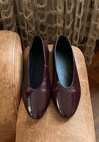 Burgundin nahkakengät kiiltävällä pinnalla, mantelin muotoisella varpaalla ja pehmeällä mustalla vuorella, aseteltuna teksturoidulle ruskealle pinnalle.