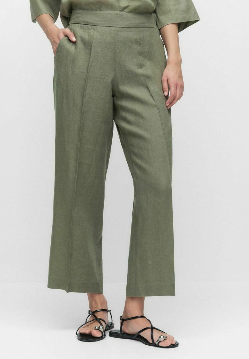 Olivgröna linnbyxor med hög midja, rak ben-design, sidofickor och subtil textur; bärs med svarta sandaler med remmar.