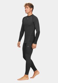 Czarny zestaw bazy sportowej z długim rękawem i dopasowanymi legginsami; obecne są teksturowane panele i akcenty z logo.